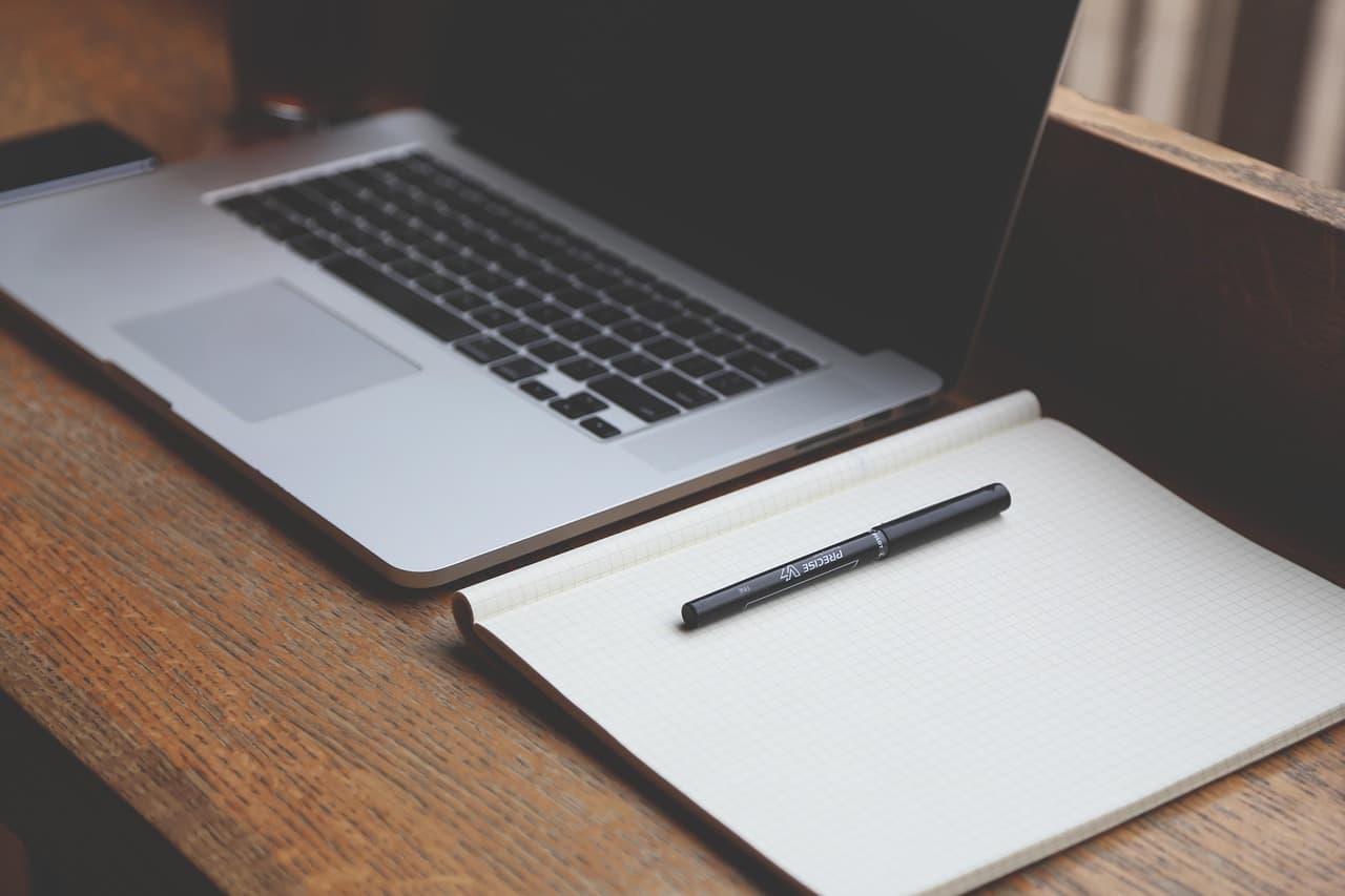 A desk with a laptop and a grid notebook used to draft a work manual